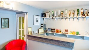 A bar area with a counter, a red chair, and a wall-mounted shelf with various bottles and glasses. - The Avenue (Shanklin)