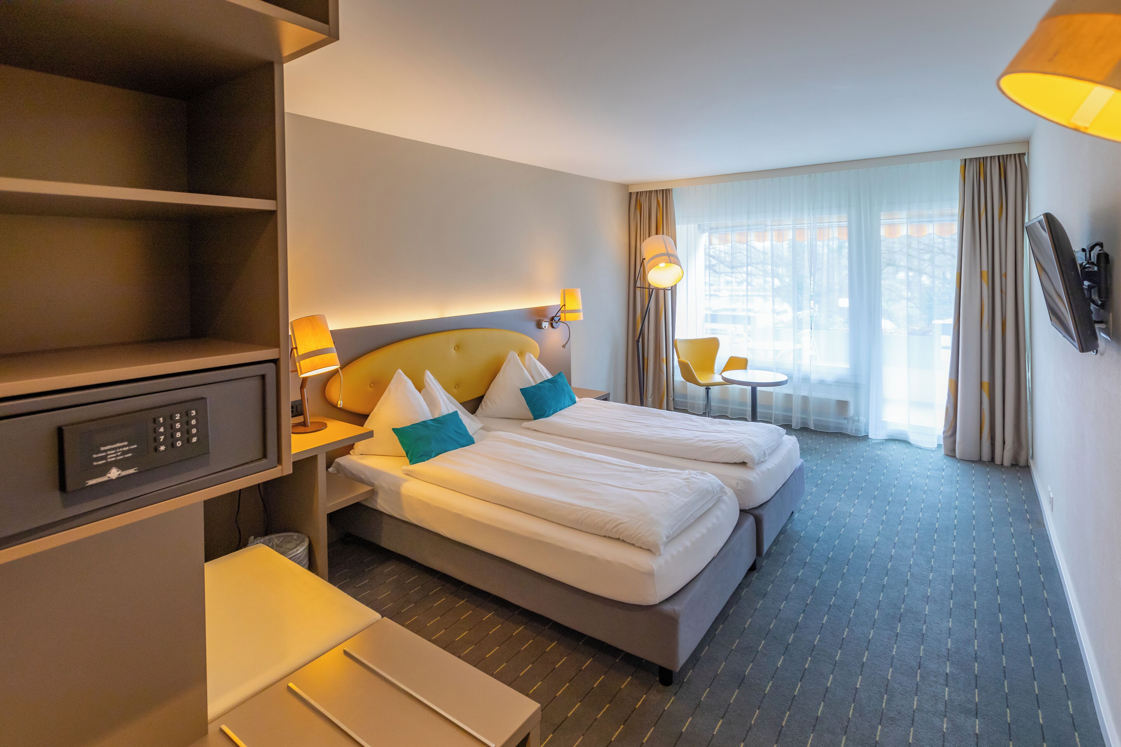 Una habitación de hotel con cama, mesitas de noche, un escritorio, una lámpara y una ventana con cortinas.