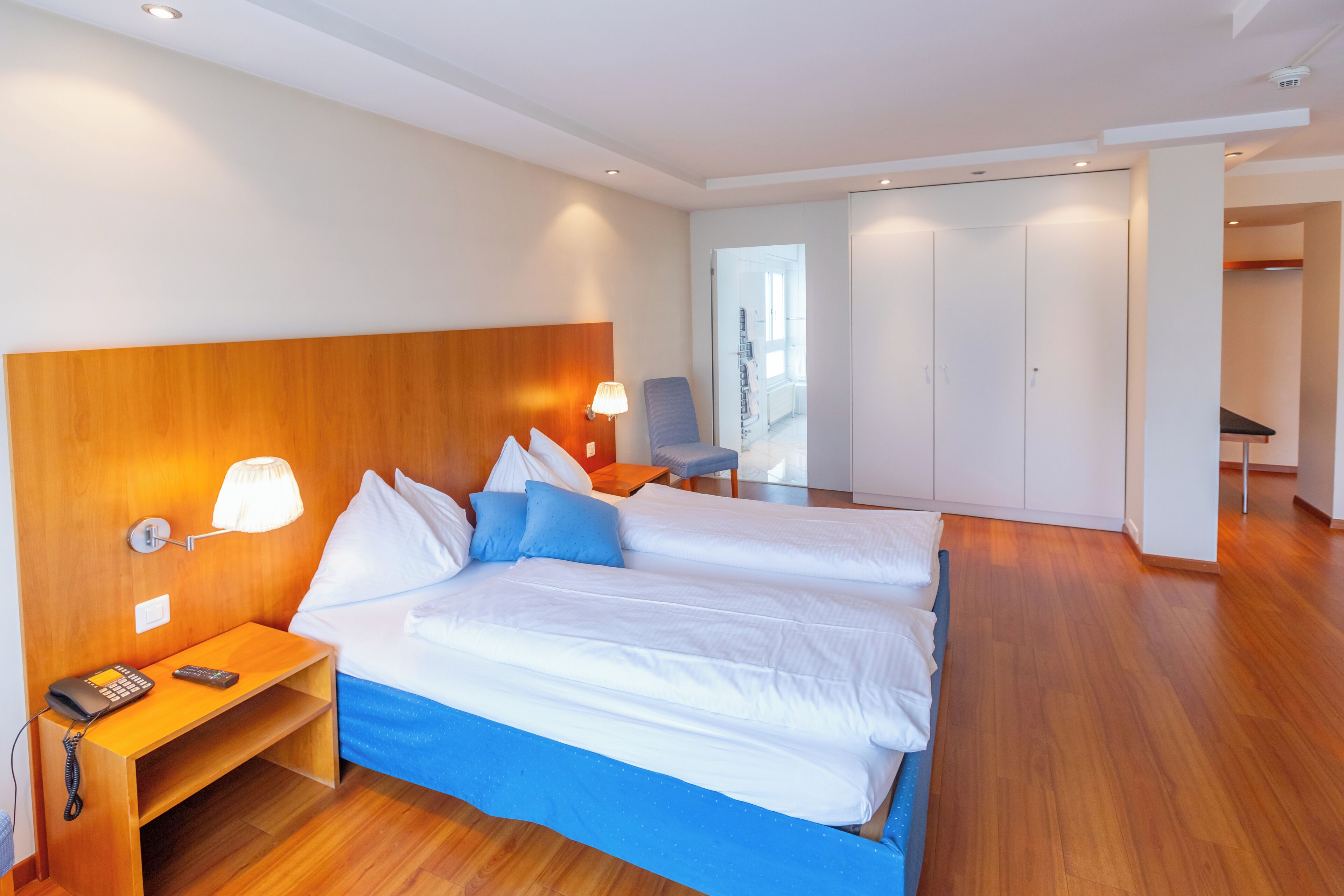A hotel room with a large bed, bedside table, lamp, and a view of the hallway.