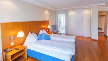 A hotel room with a large bed, bedside table, lamp, and a view of the hallway.