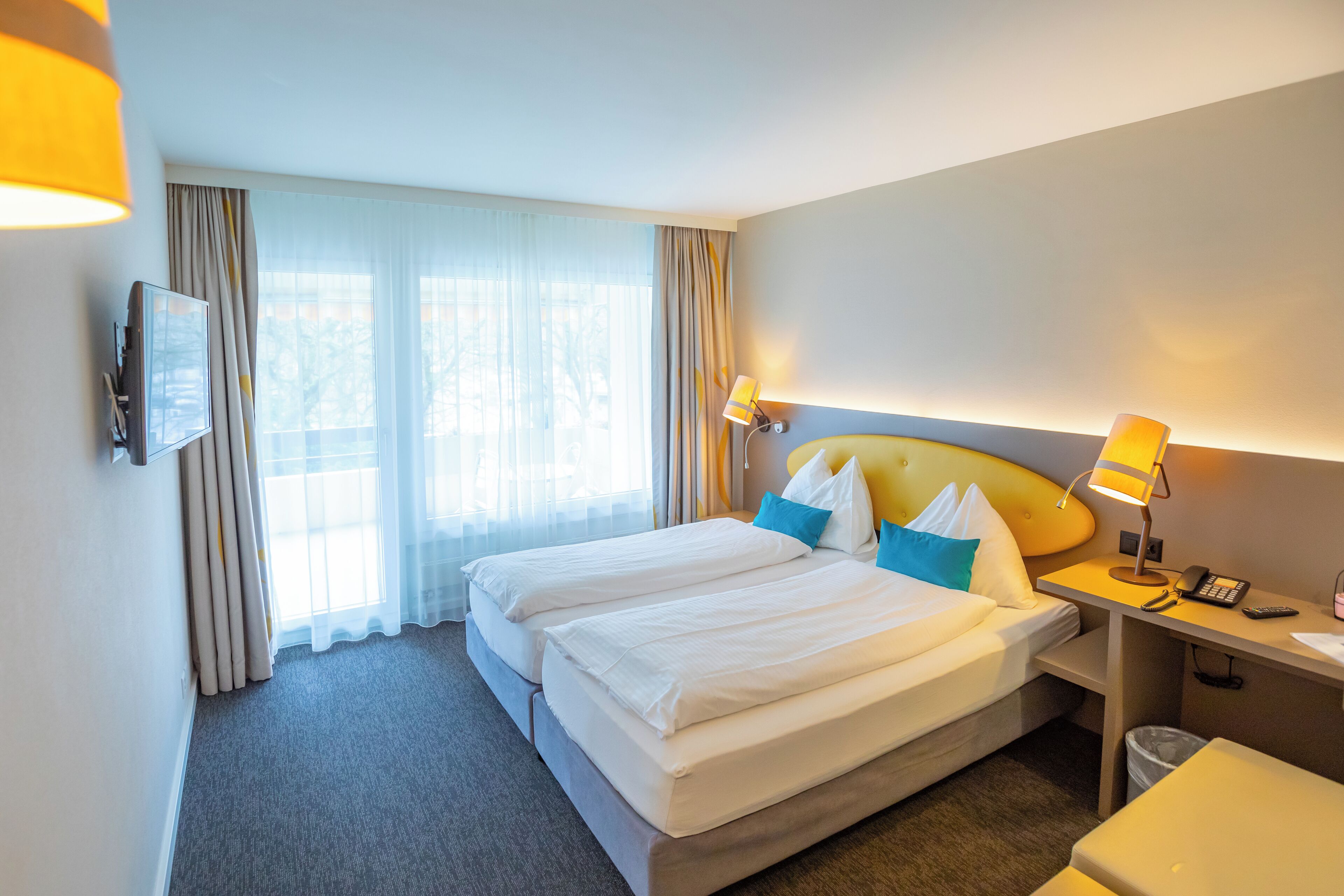 A hotel room with two beds, a desk, a chair, a TV, and a window with curtains.