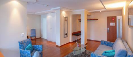 Una sala de estar moderna con una mesa de centro de vidrio, sofás con estampado y piso de madera.