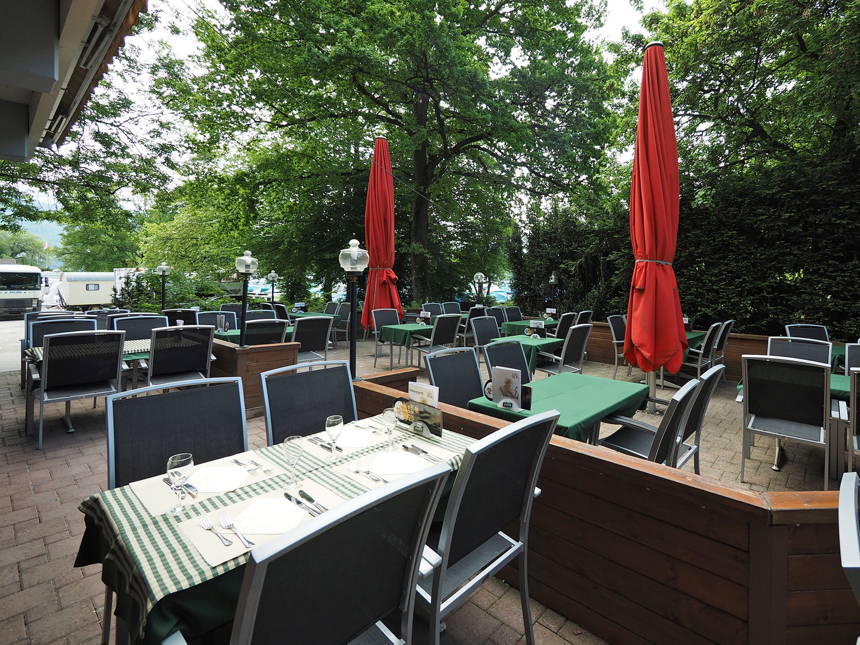 Un espace de restauration en plein air avec des tables et des chaises, des parasols rouges et un sol en briques.