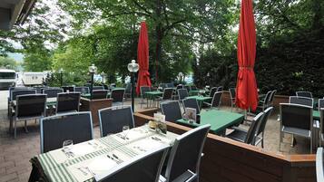 Un espace de restauration en plein air avec des tables et des chaises, des parasols rouges et un sol en briques.