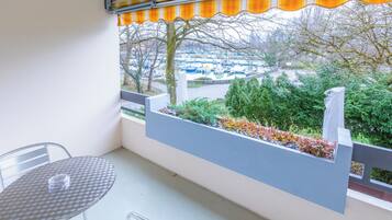 A balcony with a table and chairs, a view of a parking lot, and a row of trees.