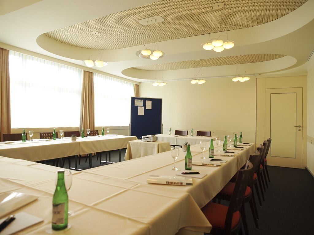 A conference room with long tables, chairs, and a white ceiling with circular light fixtures.