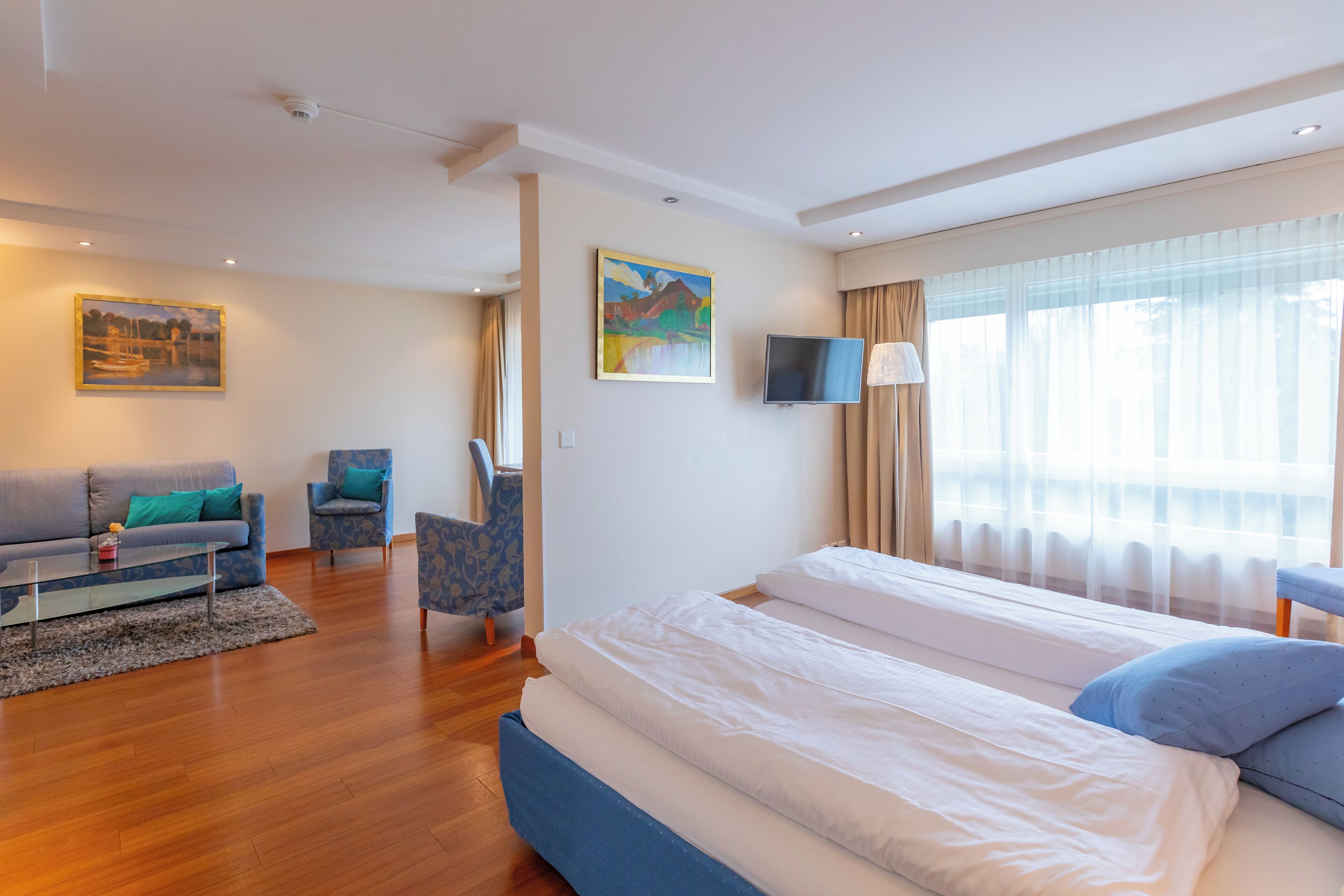 A modern hotel room with a large bed, a sofa, a chair, and a TV.