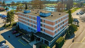 Un hôtel à plusieurs étages, avec une bande verticale bleue sur sa façade, un parking et une vue sur les montagnes et un lac.