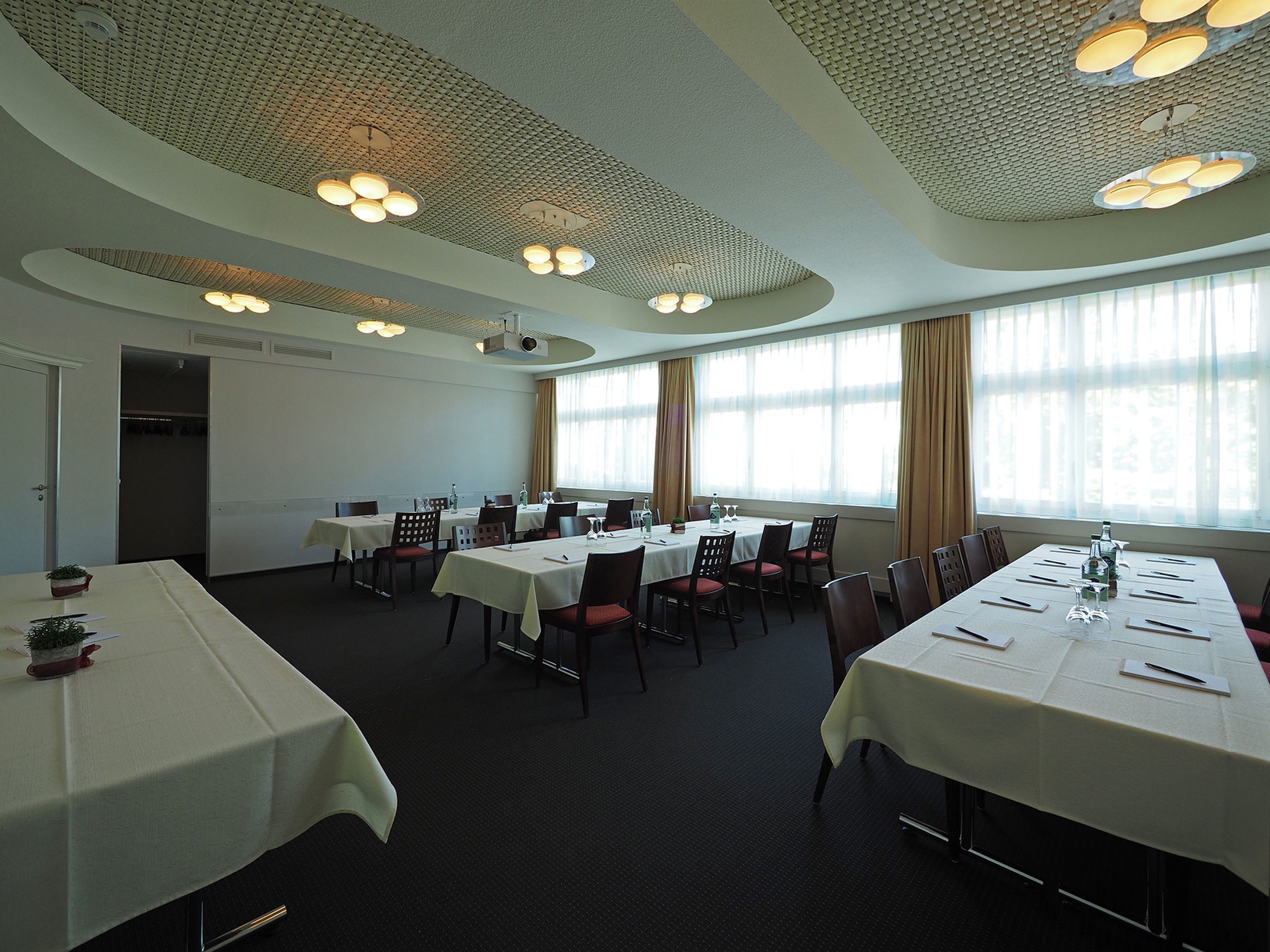 A conference room with multiple tables, chairs, and a projector screen.