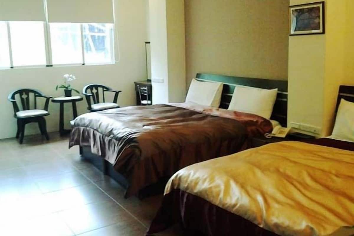 Quarto de hotel com duas camas, uma mesa pequena, duas cadeiras e uma janela.