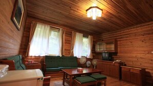 A cozy cabin interior with a wooden ceiling, a sofa, a table, a television, and a small kitchen area. - Xitou Education Center Hostel (Lugu)