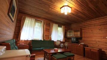 A cozy cabin interior with a wooden ceiling, a sofa, a table, a television, and a small kitchen area.