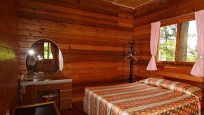 A wooden cabin room with a bed, a desk with a chair, a mirror, and a window with curtains. - Xitou Education Center Hostel (Lugu)