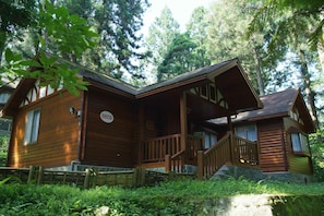 A wooden cabin with a stone foundation, a porch, and a staircase leading to the entrance. - Xitou Education Center Hostel (Lugu)