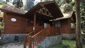 A rustic log cabin with a stone foundation, wooden porch, and a staircase leading to the entrance.
