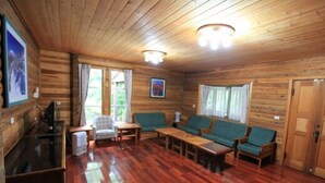 A wooden cabin interior with a wooden floor, a sofa, a chair, a table, and a television. - Xitou Education Center Hostel (Lugu)