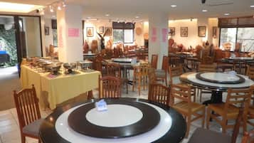 A restaurant with multiple round tables and chairs, a buffet setup, and various wall decorations.
