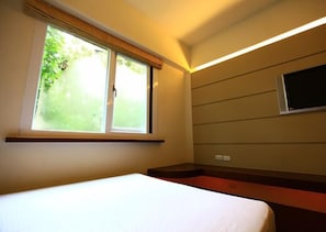 A hotel room with a bed, a window with a view of greenery, and a flat-screen TV mounted on the wall. - Xitou Education Center Hostel (Lugu)