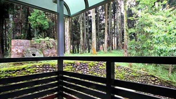 A room with a view of a forest through large windows, a black railing, and a small table with a chair. - Haoshengdi (Lugu)