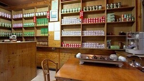 A small, wooden interior with shelves stocked with various products, a wooden table, and chairs. - Haoshengdi (Lugu)