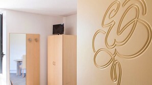 Camera d'albergo con armadio in legno, televisore sopra e parete decorata con un monogramma.