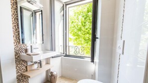 Un bagno moderno con lavandino, specchio e water bianchi. Una finestra offre vista su del verde all'esterno.
