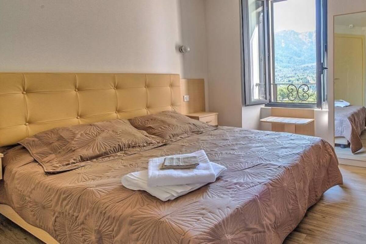 A bedroom with a large bed, a bedside table, a window with a view, and a wardrobe.
