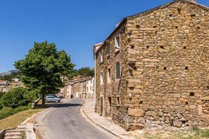 A stone building with a curved road in front, a tree, and a parked car. - Hotel A Sant'Anna (Albertacce)
