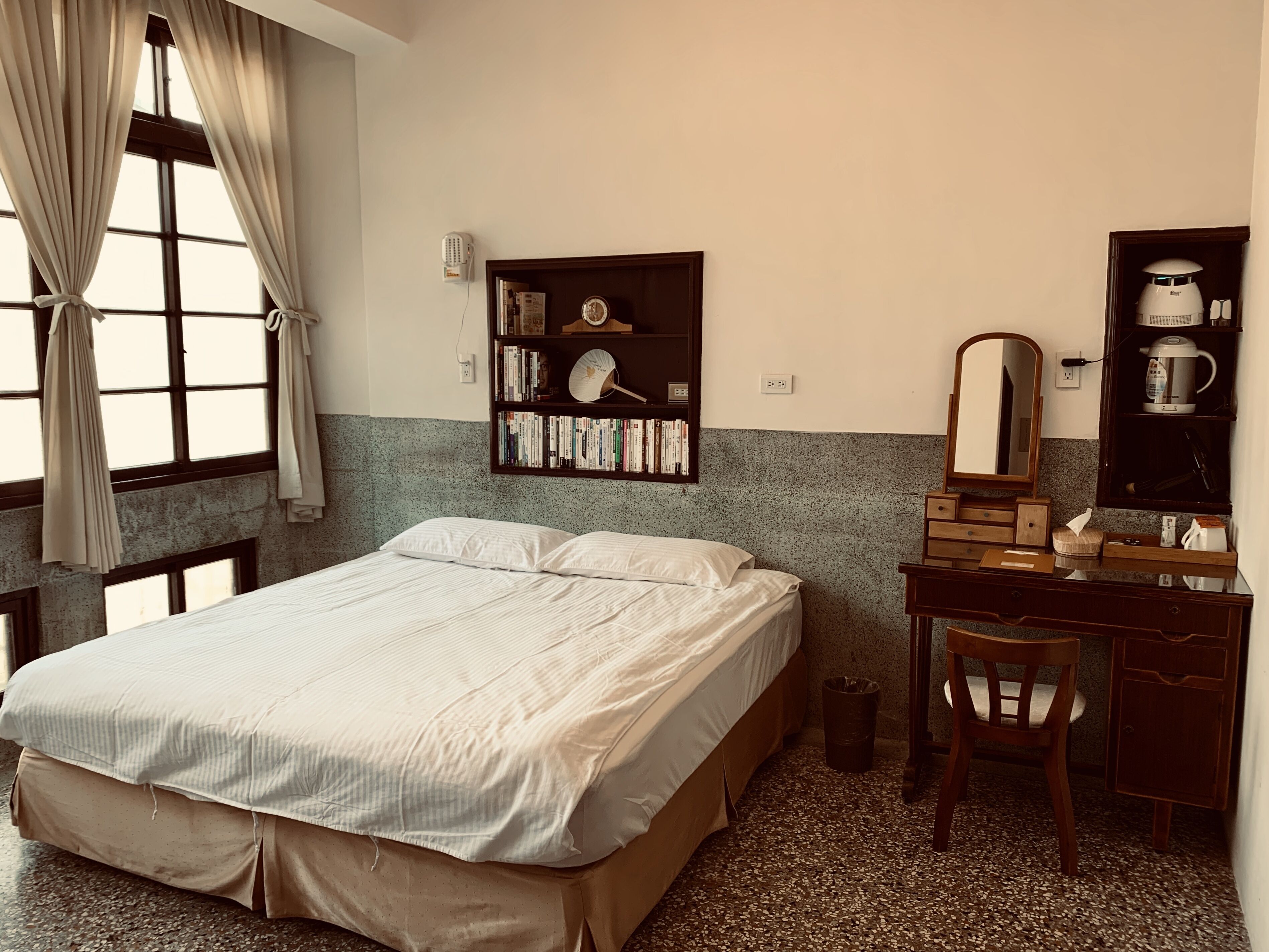 A neatly arranged bedroom with a bed, a bookshelf, a desk, and a mirror.