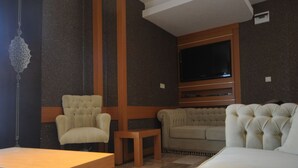 Una sala de estar con sofá, sillón y televisor montado en la pared.