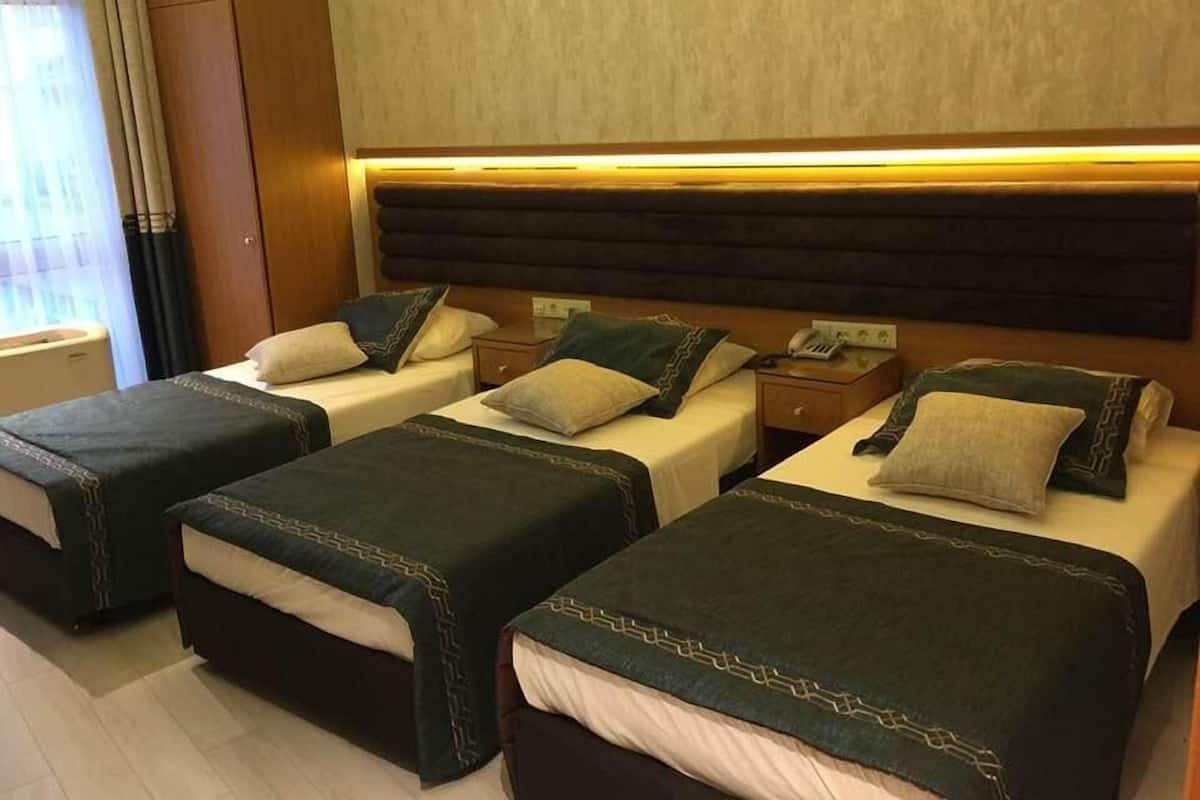 Habitación de hotel con tres camas, cada una con cubrecama verde oscuro y almohadas a juego. Hay un cabecero de madera sobre las camas y una mesita de noche con un teléfono y una lámpara.