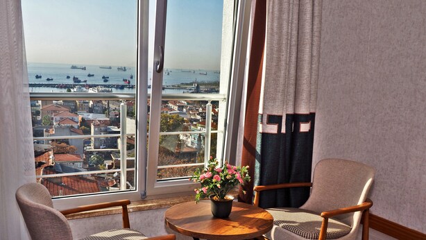 Un balcón con vistas al puerto, con dos sillas, una mesita y una planta en maceta.
