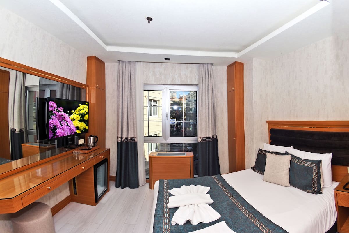 Habitación de hotel con cama, escritorio de madera, televisor de pantalla plana, cortinas y vista a edificios.