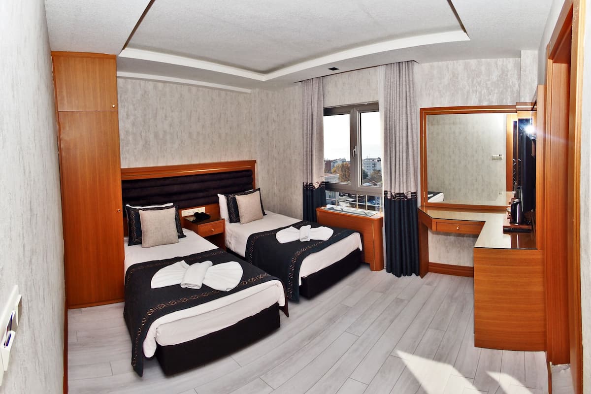Habitación de hotel con dos camas, un espejo grande, un escritorio y una ventana con vista a la ciudad.