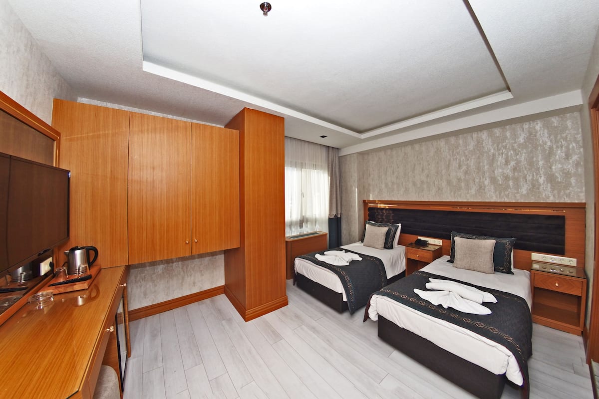 Habitación de hotel con dos camas, un armario de madera, un escritorio con cafetera y un televisor.