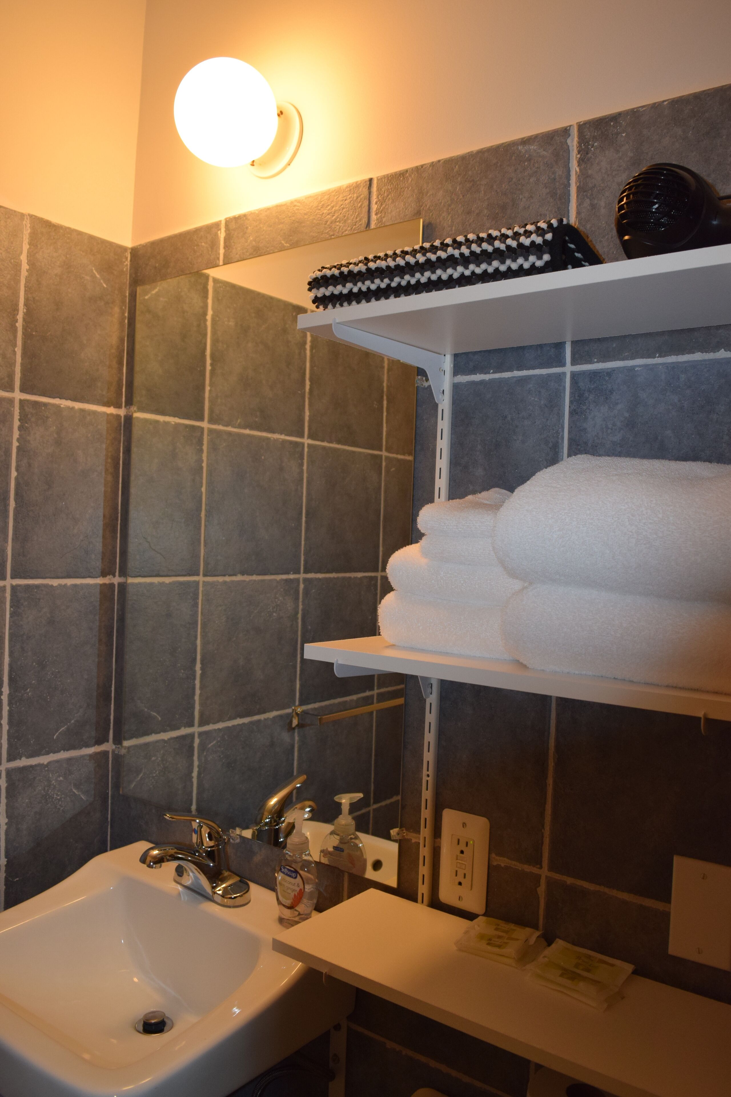 A bathroom with a white sink, a mirror, and a shelf with towels and a hairdryer.