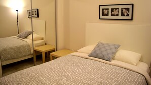 A hotel room with two beds, a bedside table, a chair, a floor lamp, and framed pictures on the wall. - Detroit Vacation Rental (Hamtramck)
