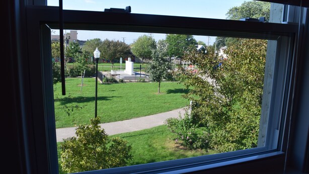 A view through a window of a grassy area with a path, a lamppost, and some trees. - Detroit Vacation Rental (Hamtramck)
