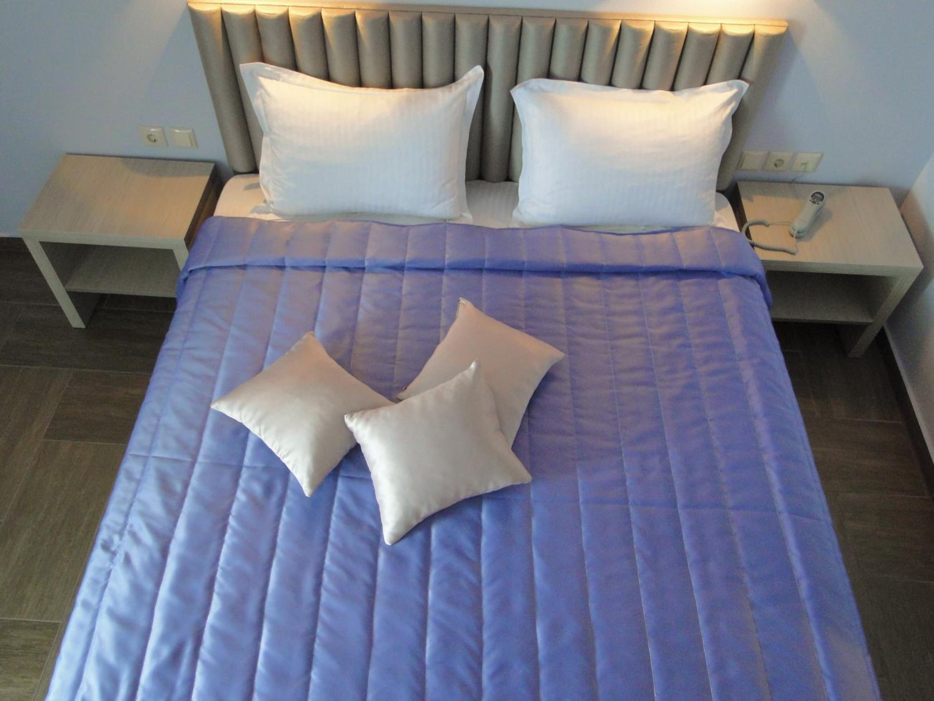 Ein ordentlich bezogenes Bett mit einer blauen Steppdecke und zwei Kissen, ein Nachttisch mit einem Telefon und eine Steckdose.