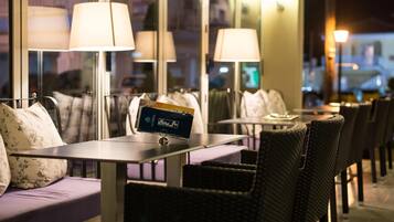 Un restaurante con terraza, que incluye una mesa con portaletras y un banco con cojines.