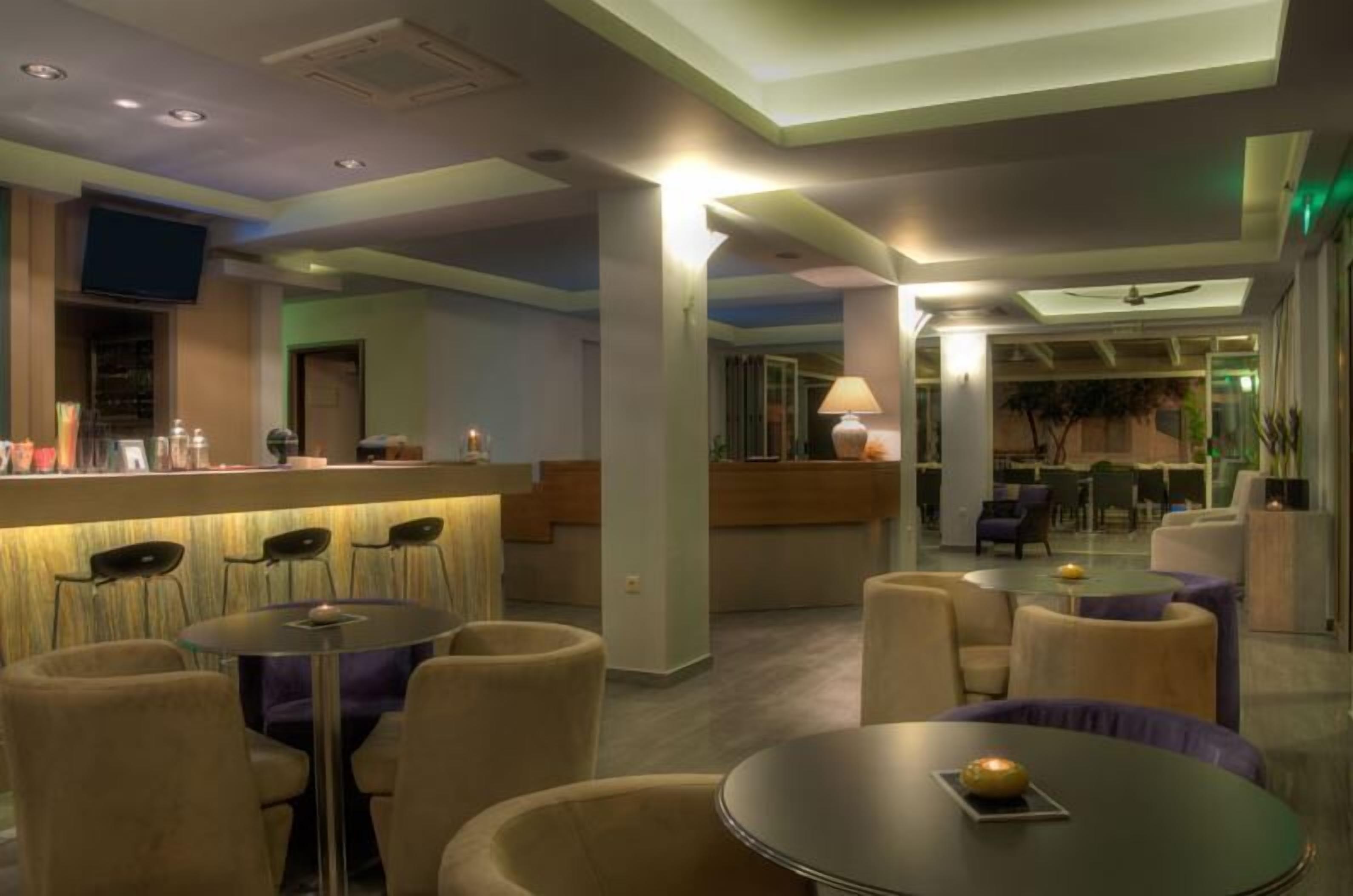 Un vestíbulo de hotel con zona de bar, arreglos de asientos y un televisor montado en la pared.