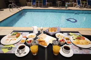 A breakfast setup by a poolside with plates of food, drinks, and a basket of bread. - Hotel Olympos (Dio-Olympos)