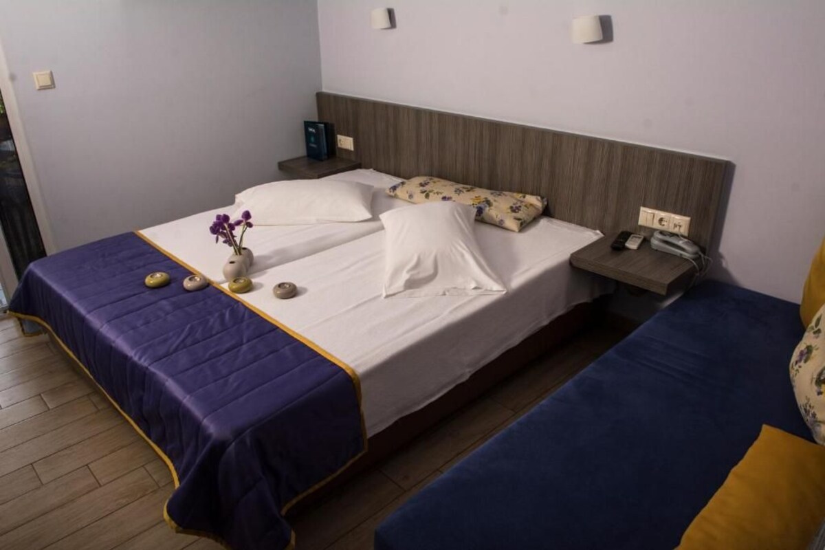 Quarto de hotel com cama, mesa de cabeceira e pequena escrivaninha com cadeira.