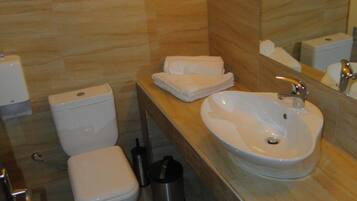 A modern bathroom with a toilet, bidet, and sink. There is a towel rack above the sink and a trash can beside the toilet.