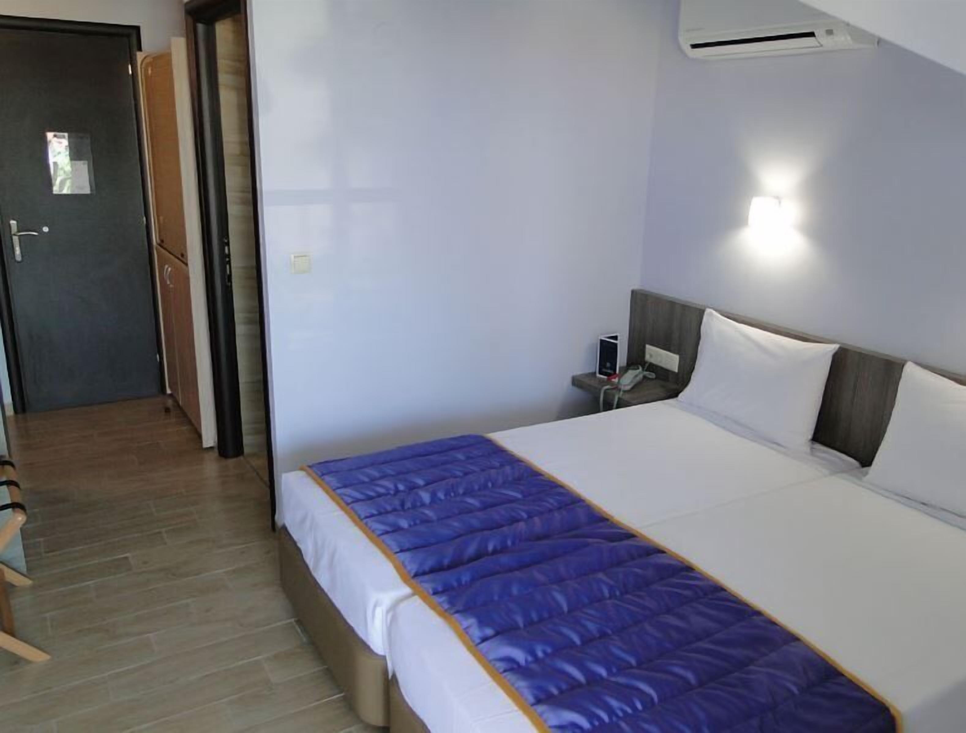 A hotel room with a bed, bedside table, and an air conditioning unit.