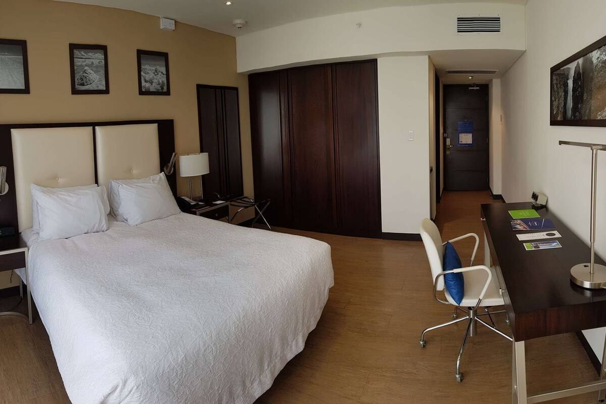 Ein Hotelzimmer mit einem großen Bett, Nachttischen, einem Schreibtisch, einem Sessel und einem Kleiderschrank.