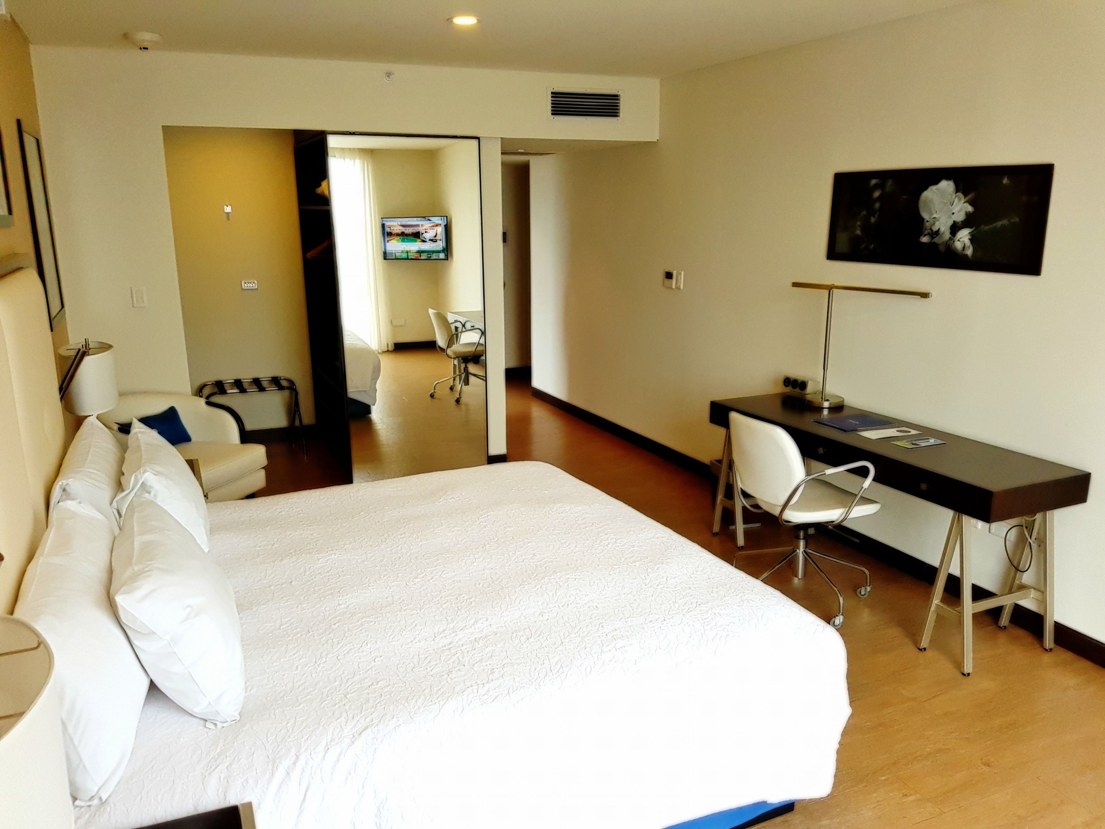 A hotel room with a large bed, a desk, a chair, a TV, and a picture on the wall.