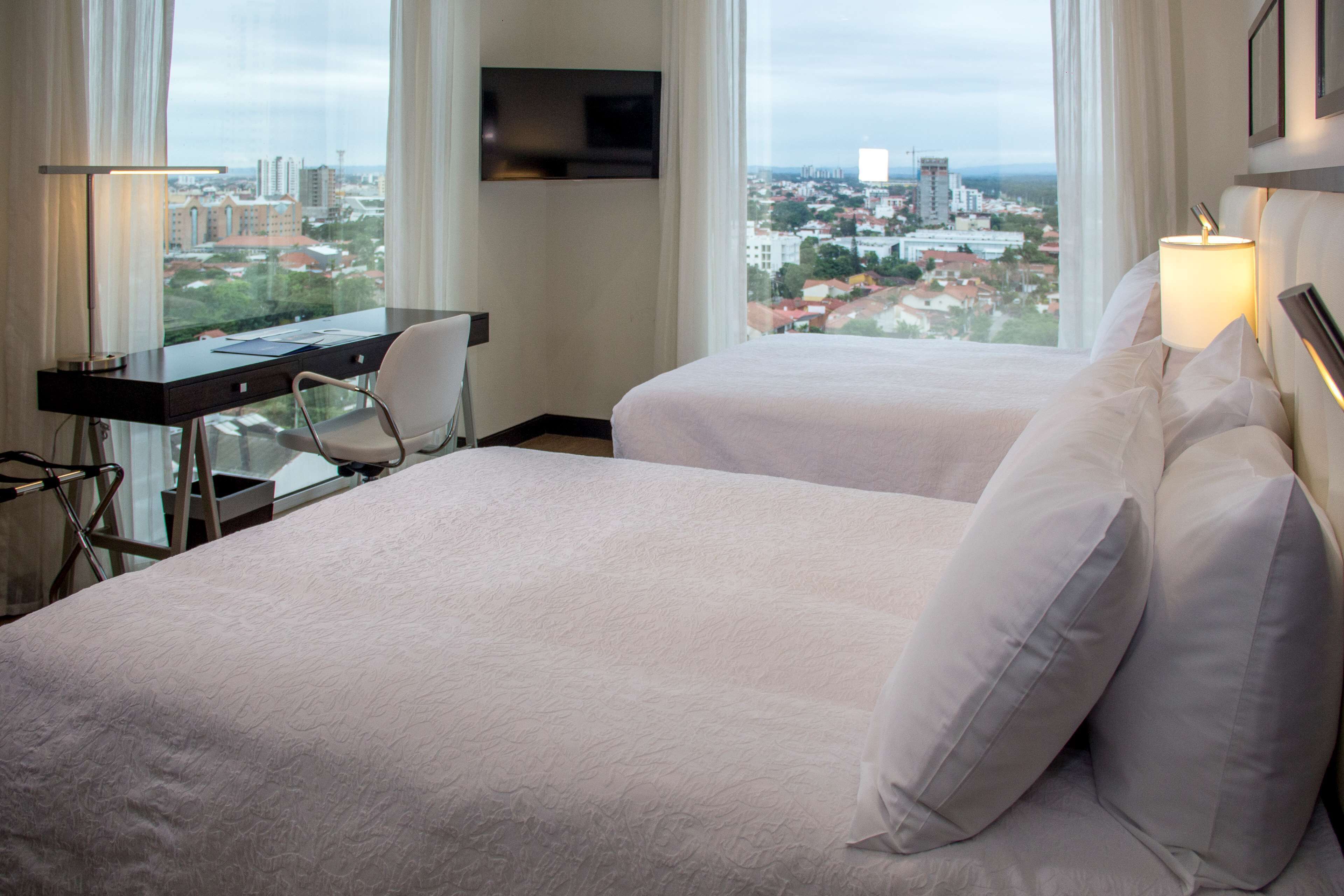 Ein Hotelzimmer mit zwei Betten, einem Schreibtisch, einem Sessel und einem Fernseher an der Wand.