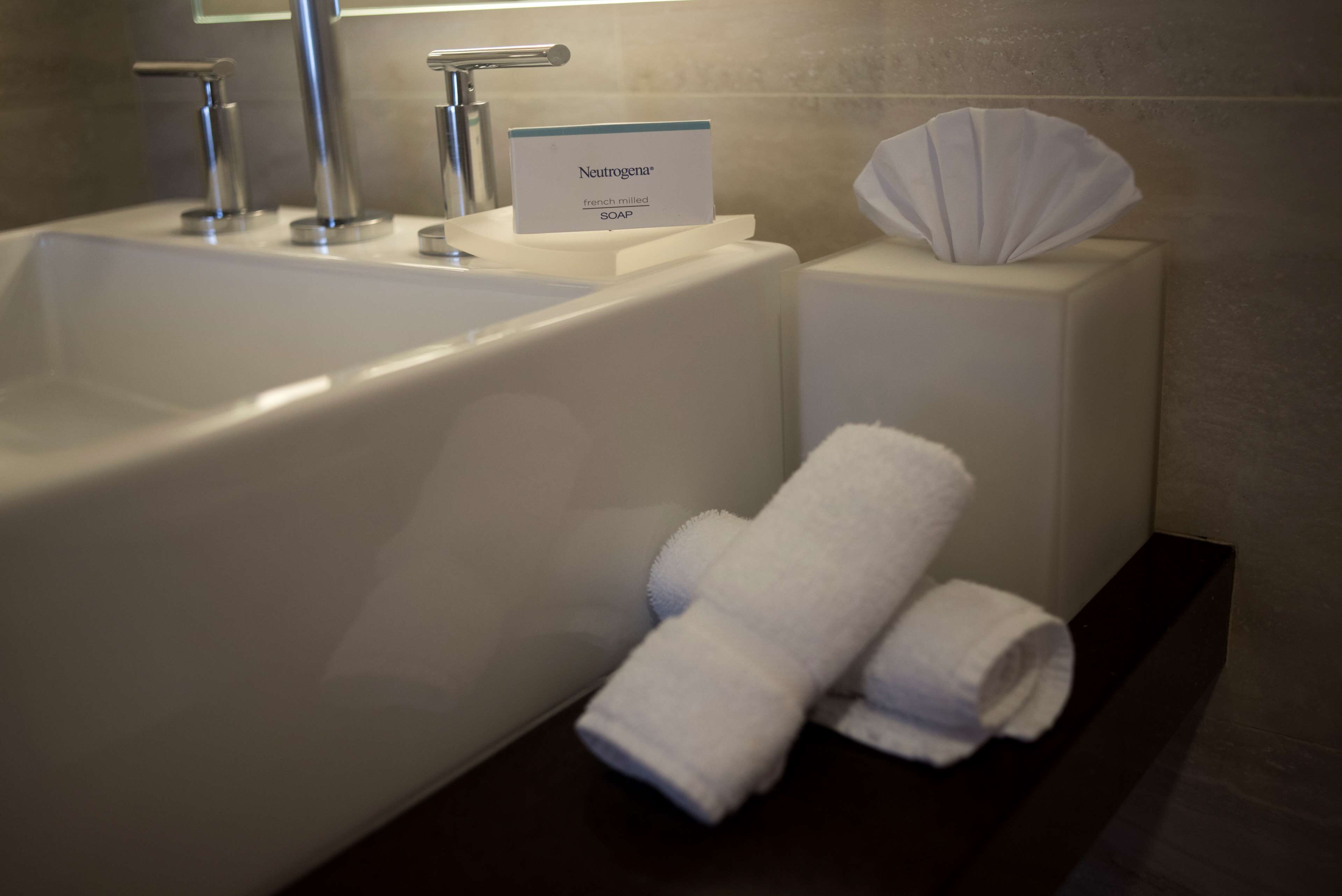 A bathroom with a large bathtub, a hand soap dispenser, and neatly folded white towels on a shelf.