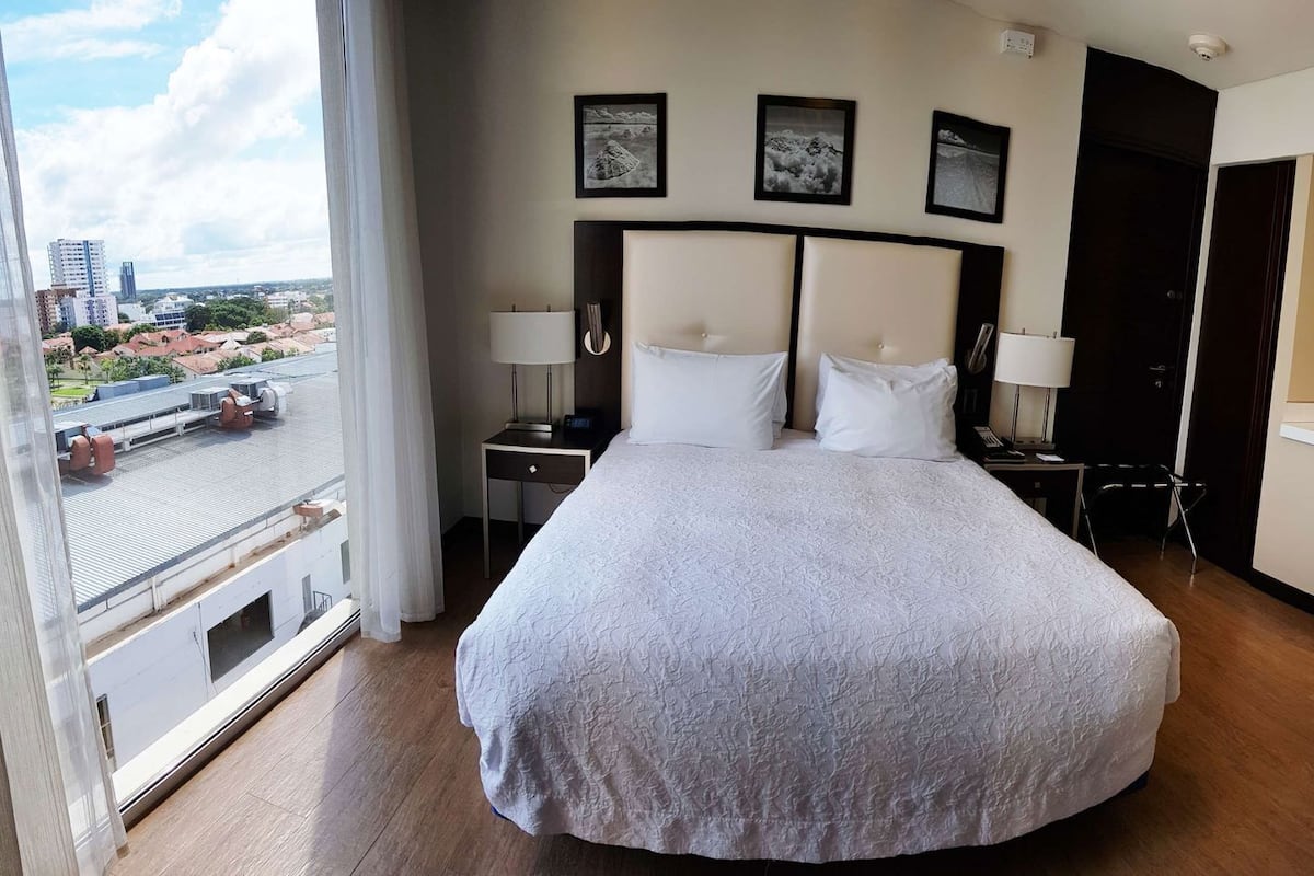 Ein Hotelzimmer mit einem großen Bett, Nachttischen, einem Schreibtisch und Blick auf die Stadt.